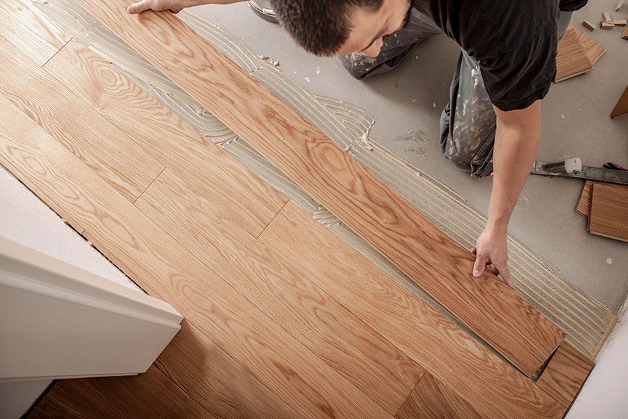 Mann verlegt Parkettdielen auf einem Estrichboden mit Kleber.