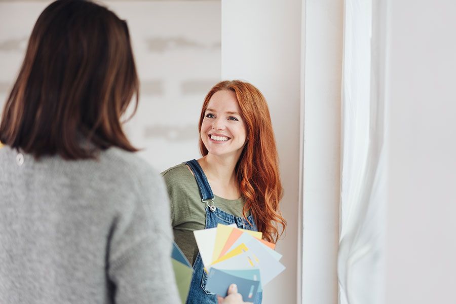 Glückliche, rothaarige Frau hält Farbmuster und spricht mit einer Person.